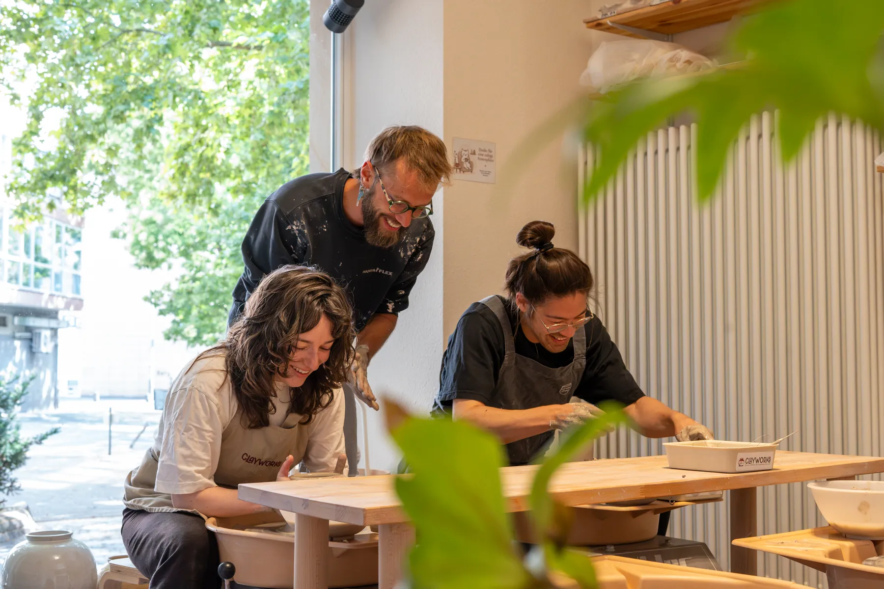 Kursleiter zeigt zwei Teilnehmerinnen an der Drehscheibe das Drehen im Clayworks Mainz